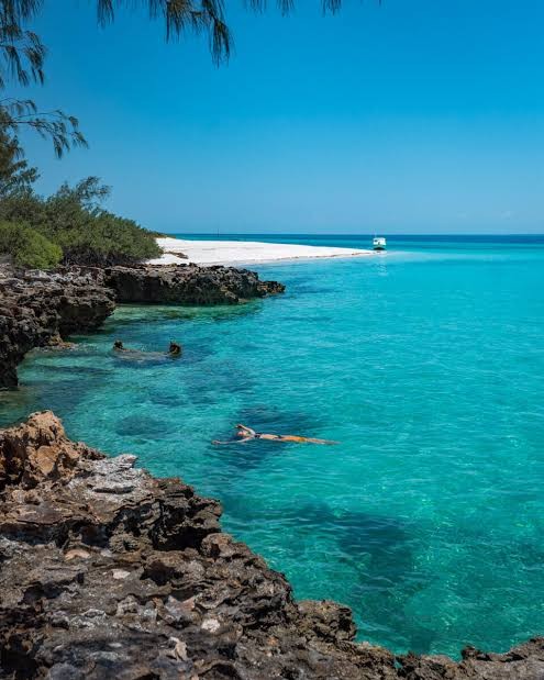 A guest snorkeling in the turquoise lagoon beside the rocky shoreline of Benguerra Island