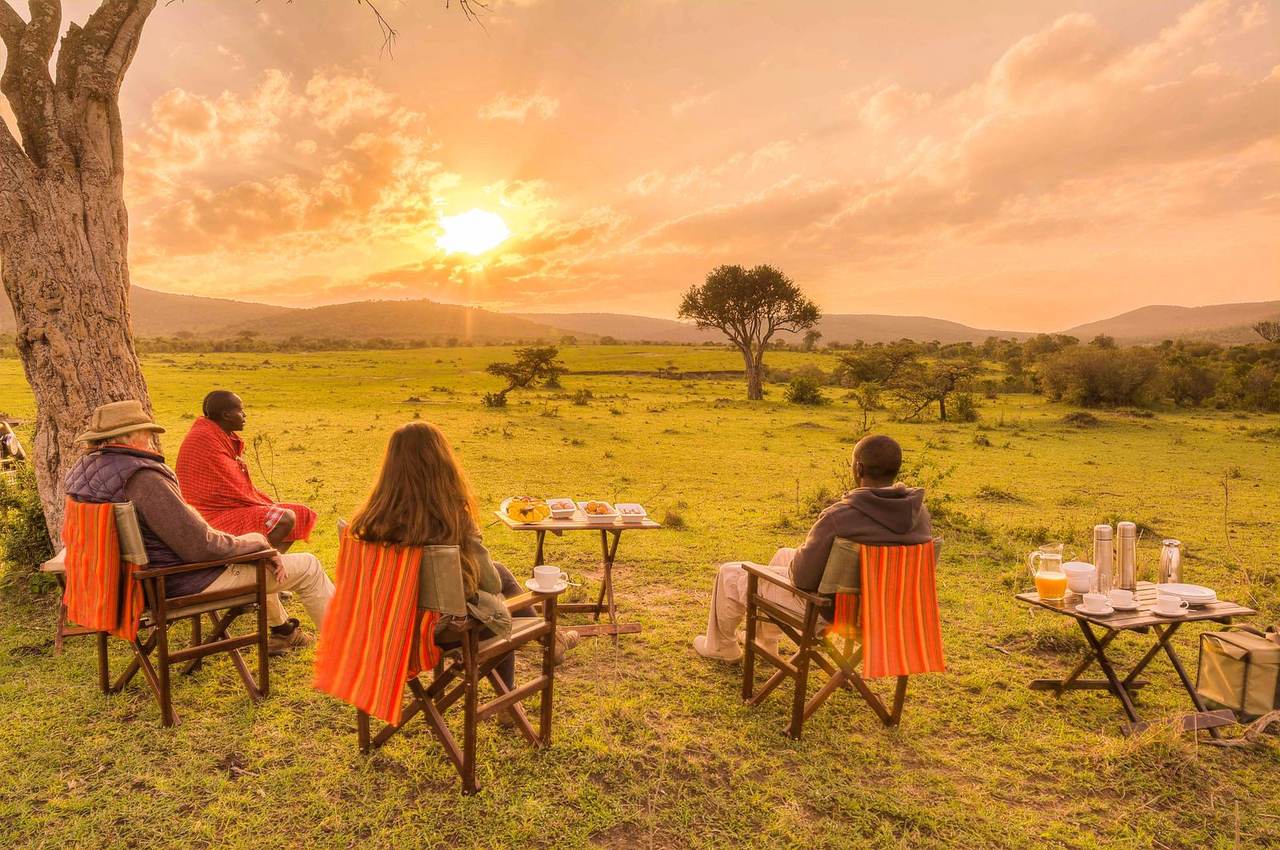 Guests and a private safari guide enjoying a bush breakfast at sunrise, part of an all-inclusive African safari