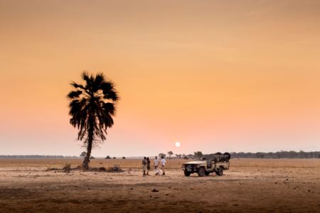 A private safari vehicle and guests at sunset on a mobile camping safari in Africa
