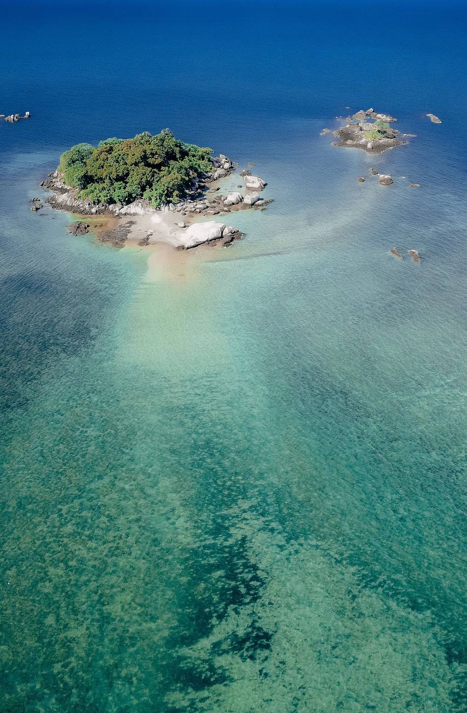 Aerial view of a small forested island surrounded by Lake Malawi's clear reef-like shallows