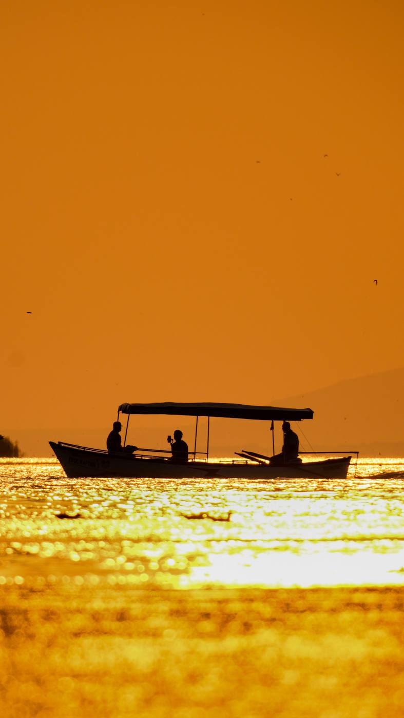 A small boat crossing Lake Malawi under a golden sunset sky