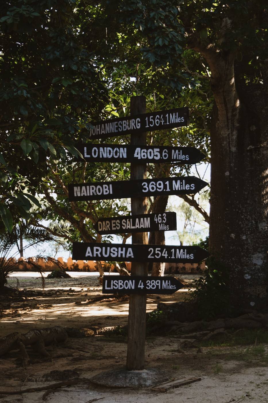 A rustic signpost marking distances to Nairobi, Arusha and Dar es Salaam near a Lake Malawi lodge